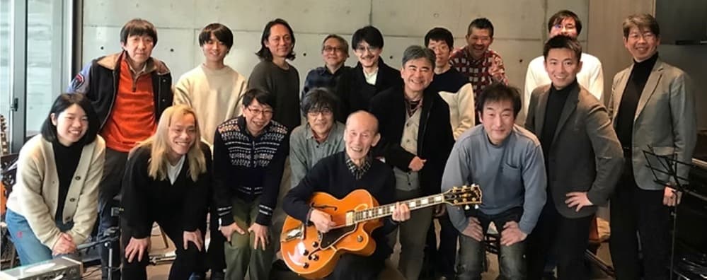 輪になって集まった人たち。中央でギターを持つ人と、周囲の参加者